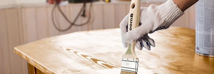 Person lackiert einen Holztisch.